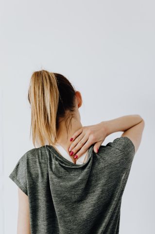 Back view of blond faceless lady in casual t shirt and manicure demonstrating pain spot on back while sitting near white wall